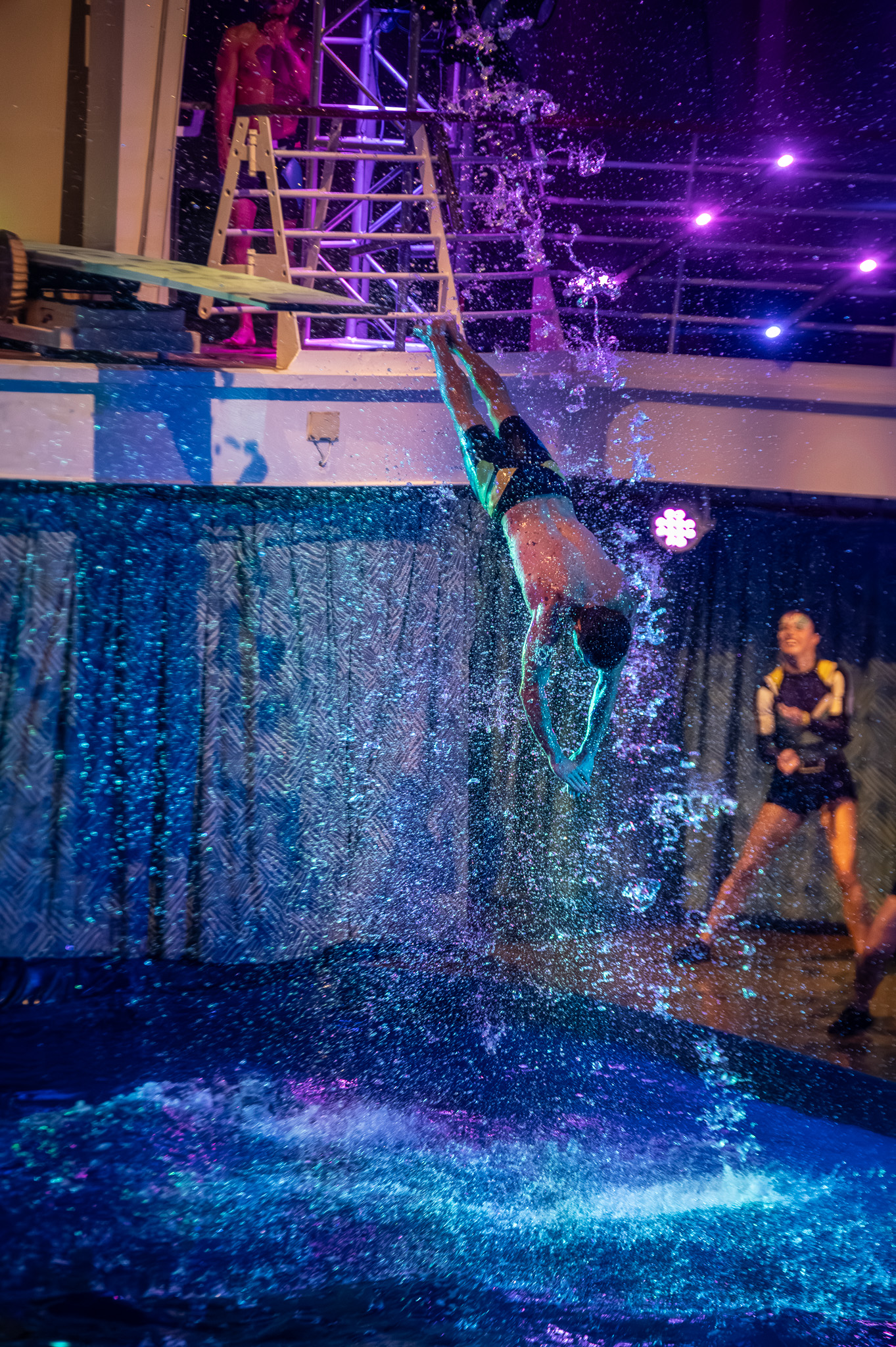 Aerial performer diving from a high platform with stage lighting