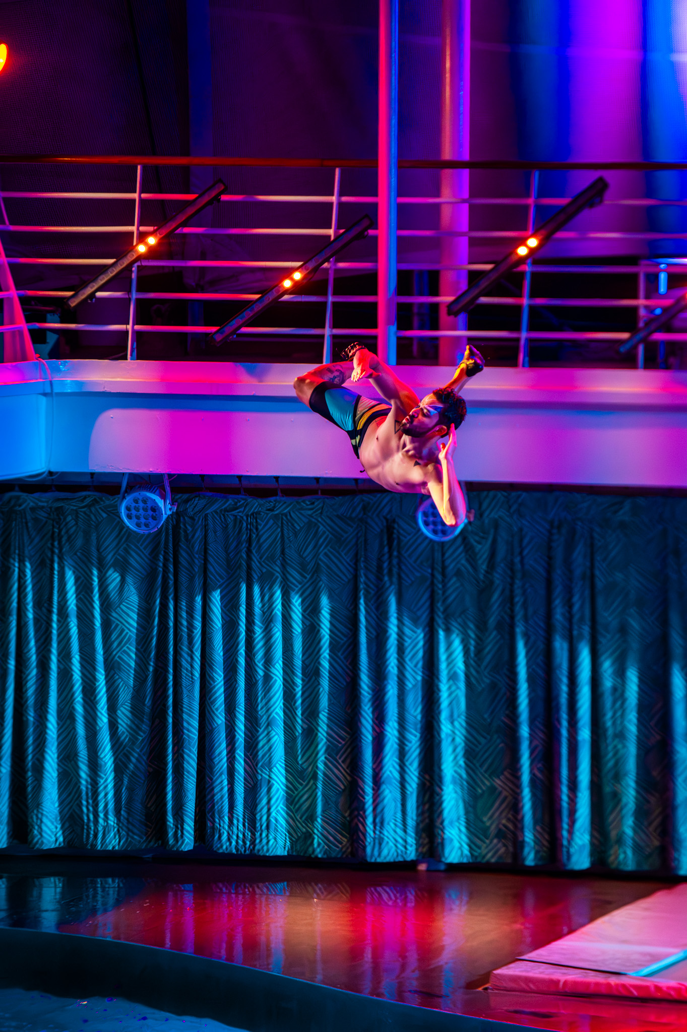 Acrobatic performer launched above the water with blue lighting