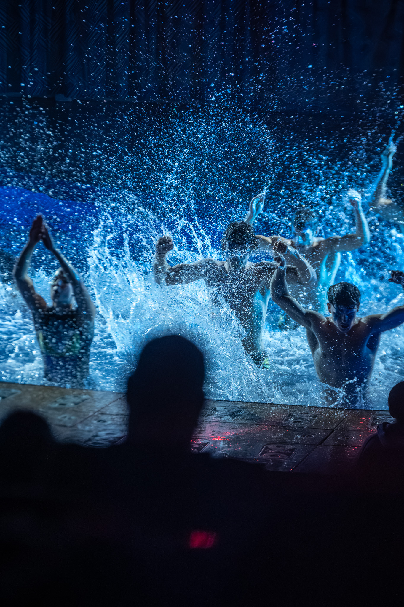 Aquatic dancers moving across the water in blue light