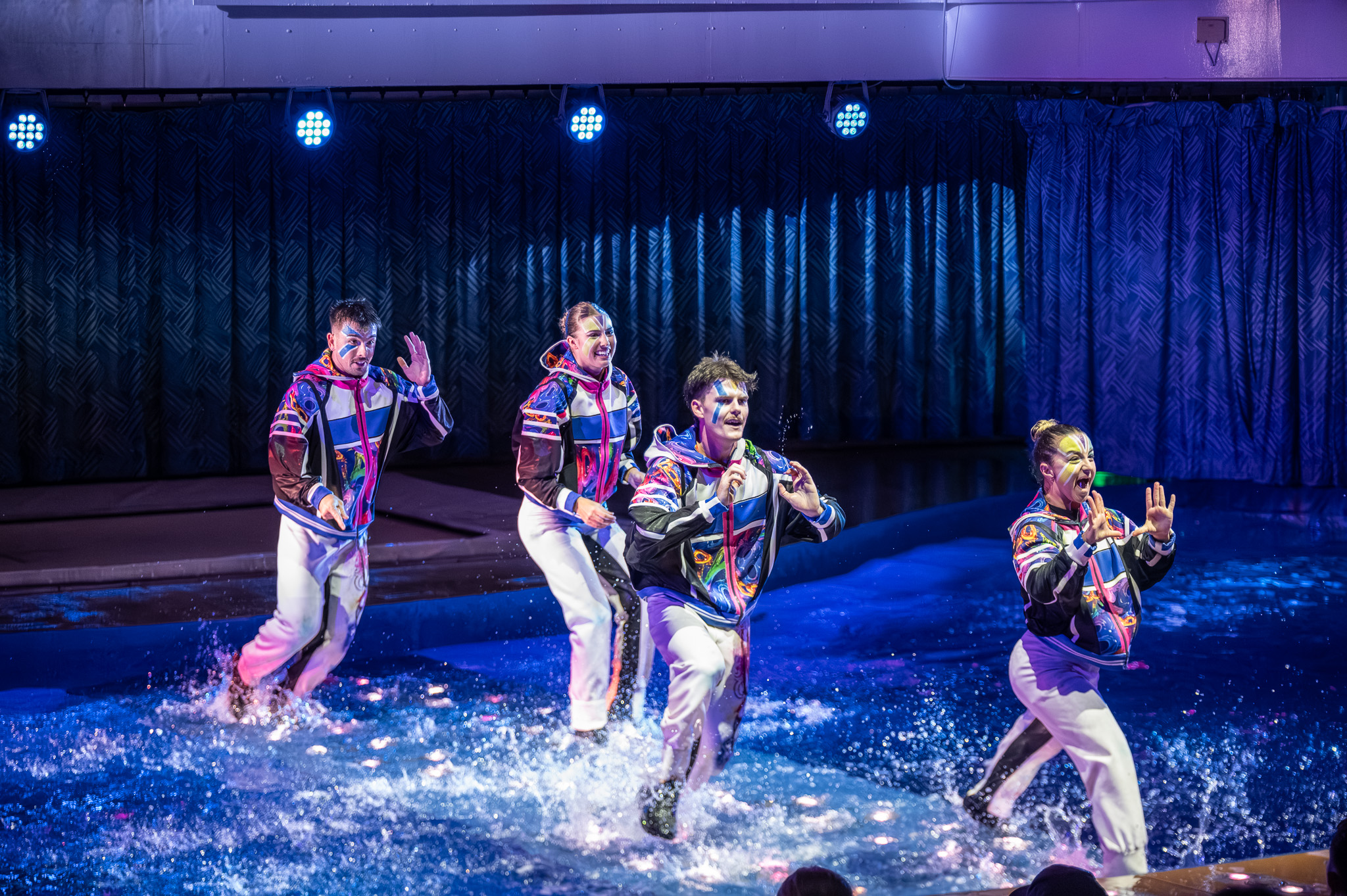 Performer suspended above the water with blue-green light